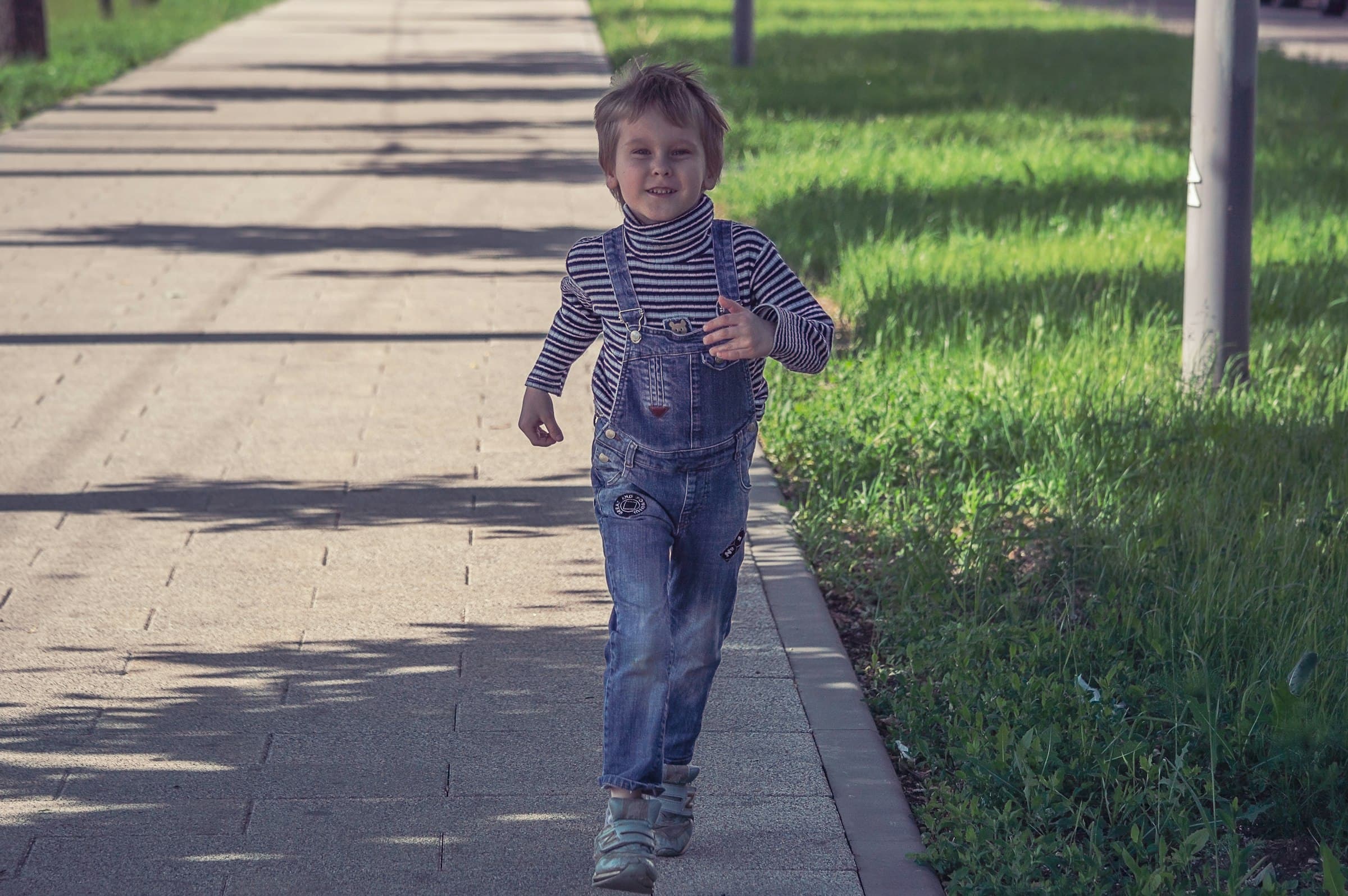A young boy running along a sunlit street
